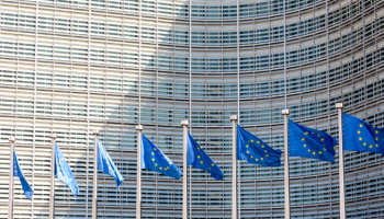 A row of flags of the European Union flying in the wind in front of the Berlaymont building, seat of the European Commission in Brussels, Belgium.